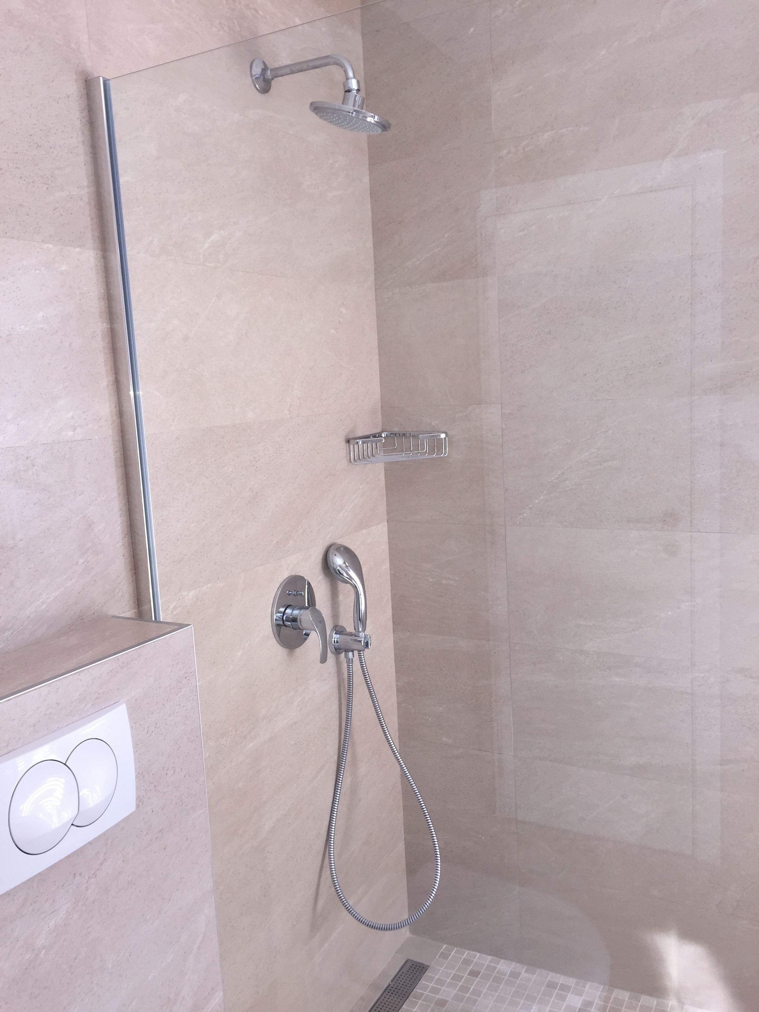 A modern shower with a handheld showerhead, a fixed showerhead, and a handheld shower hose.