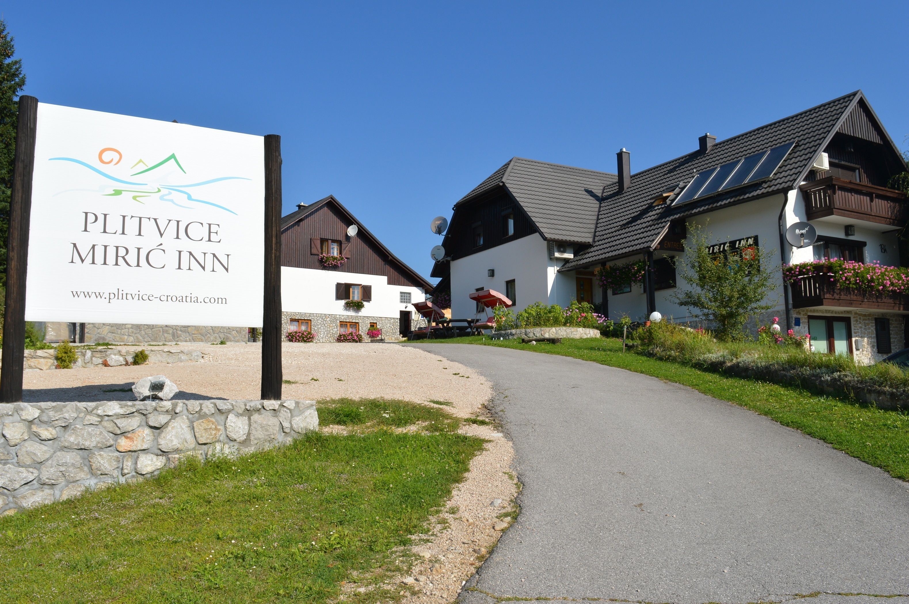 A sign for Plitvice Mirici Inn with a clear view of the surrounding buildings and a gravel path leading to the entrance.