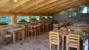 A restaurant with wooden tables and chairs, stone walls, and large windows overlooking greenery. - Plitvice Miric Inn (Plitvicka Jezera)