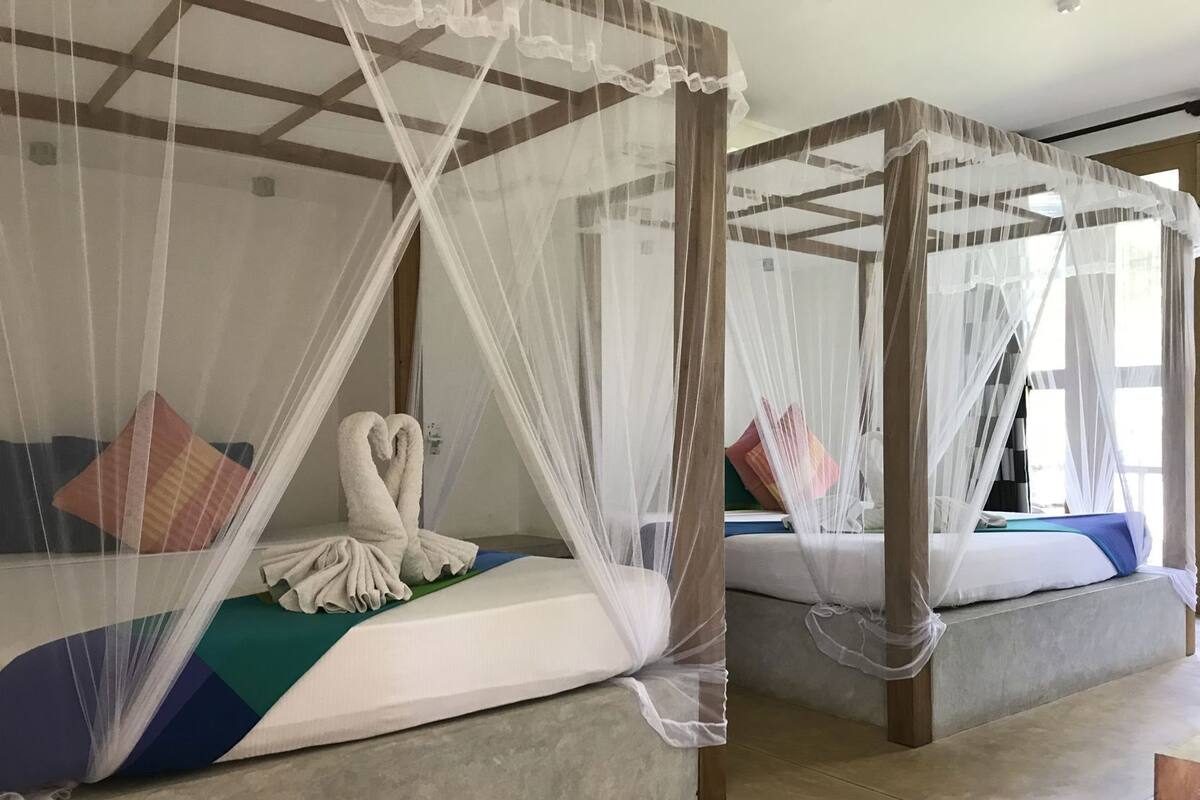 A room with four beds, each with a canopy bed and a heart-shaped towel on one bed.