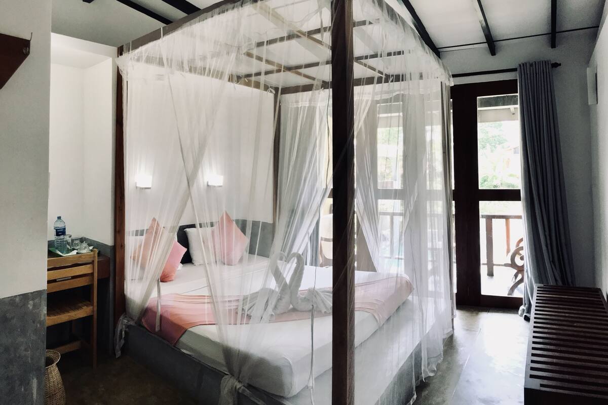 A room with a four-poster bed, a small table with a water bottle, and a bench.