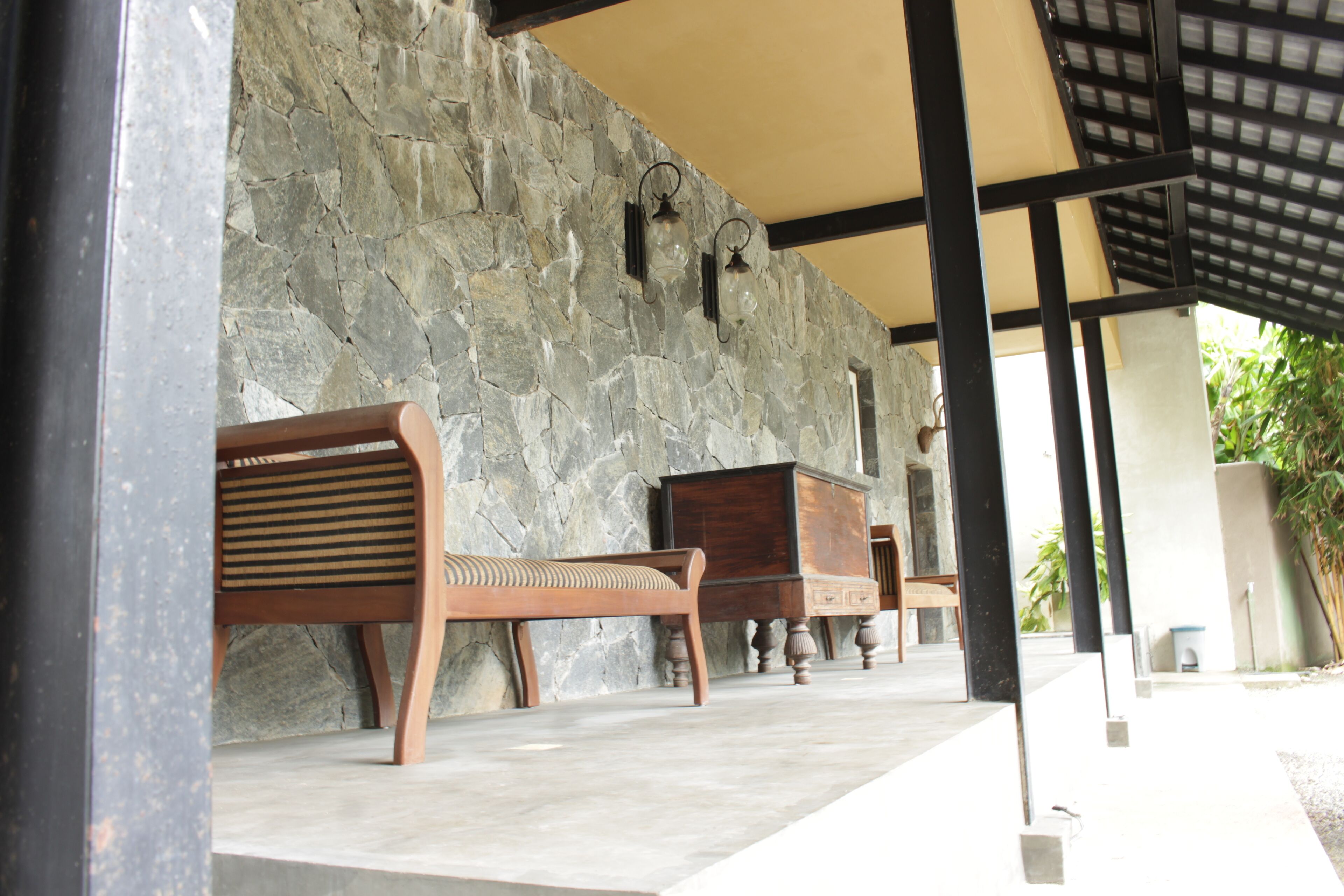 Un espacio de estar al aire libre con techo, paredes de piedra y mobiliario de madera.