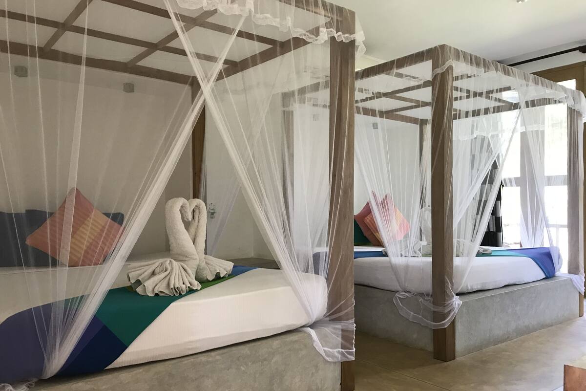 Two four-poster beds with white canopies, colorful pillows, and a heart-shaped towel on one bed.