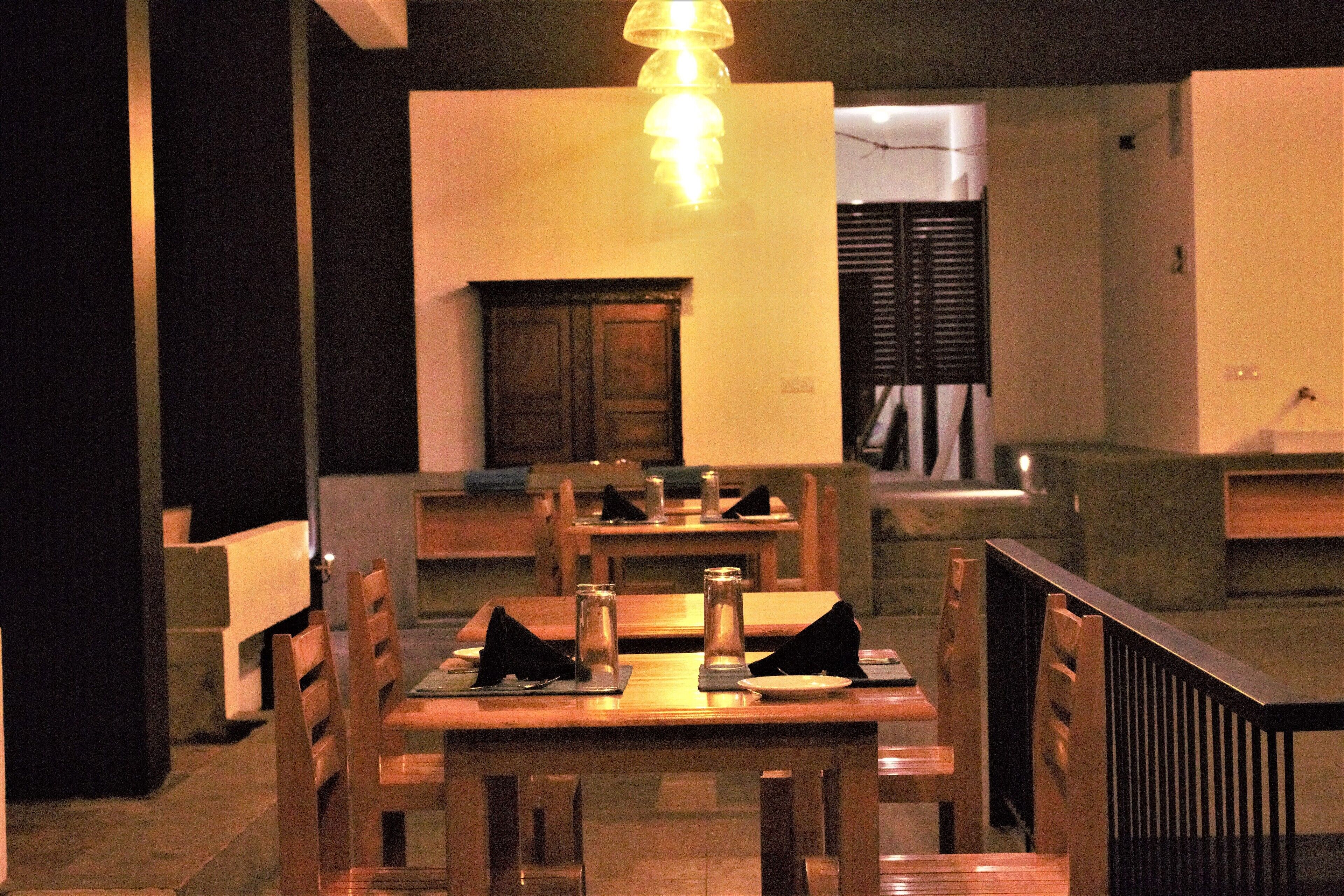 Un espace repas avec des tables et des chaises en bois, une cheminée centrale et un luminaire suspendu.