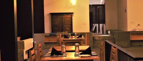 Un espace repas avec des tables et des chaises en bois, une cheminée centrale et un luminaire suspendu.