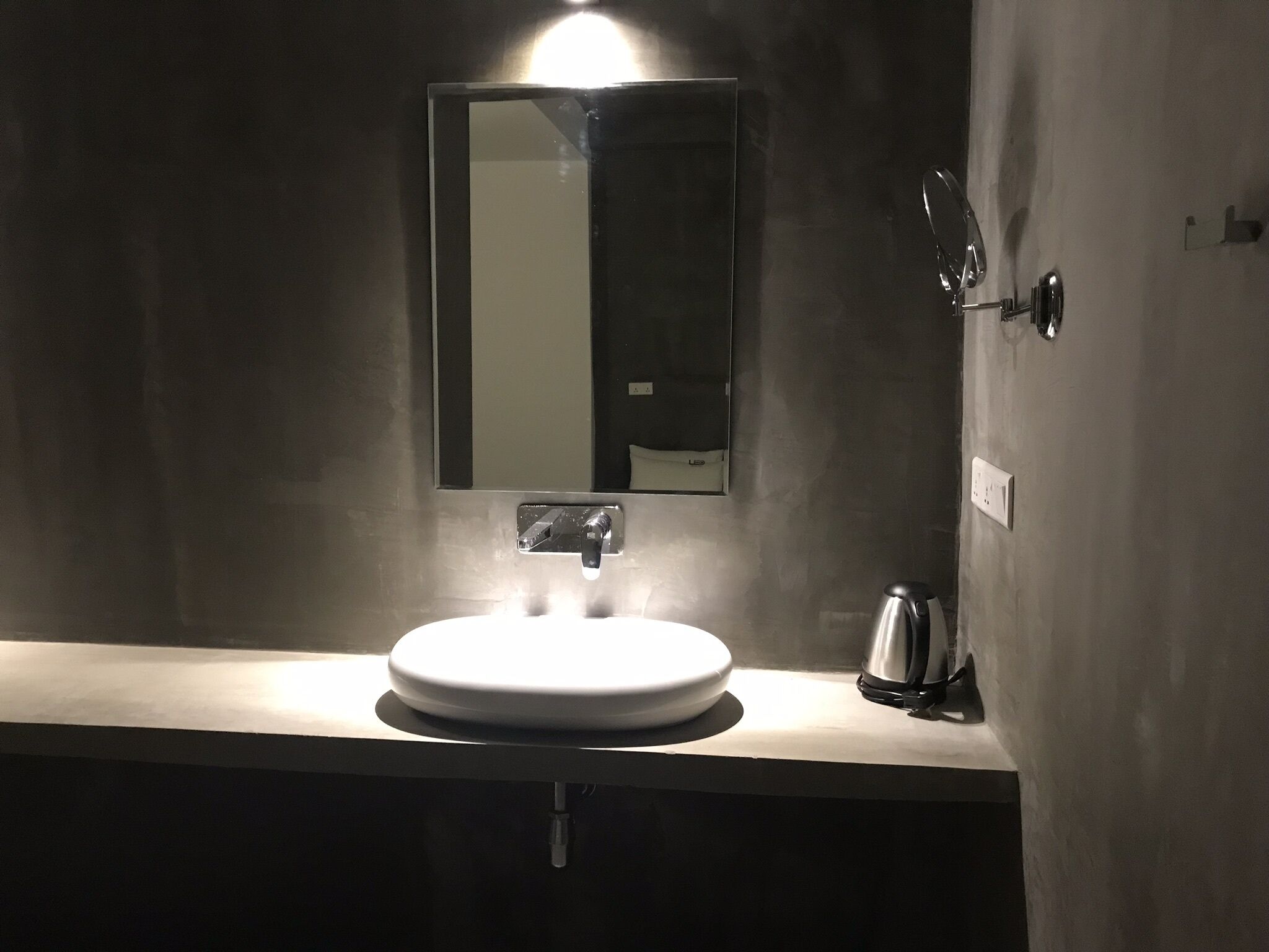 Une salle de bain moderne avec un lavabo rond, un miroir et une bouilloire.