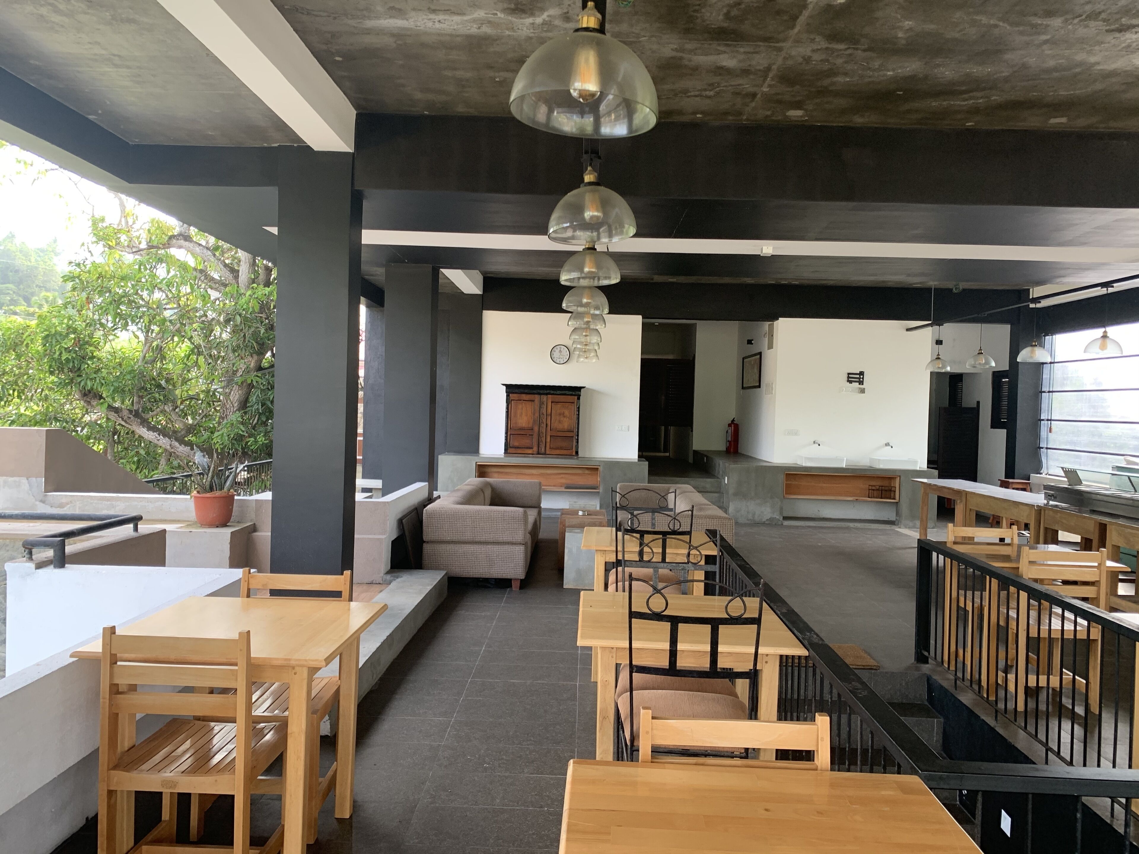 Een modern café met houten tafels en stoelen, een trap en uitzicht op groen.