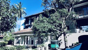 A two-story building with a tiled roof, large windows, and a balcony. There is a tuk-tuk parked in front. - Handagedara Resort (Mirissa)