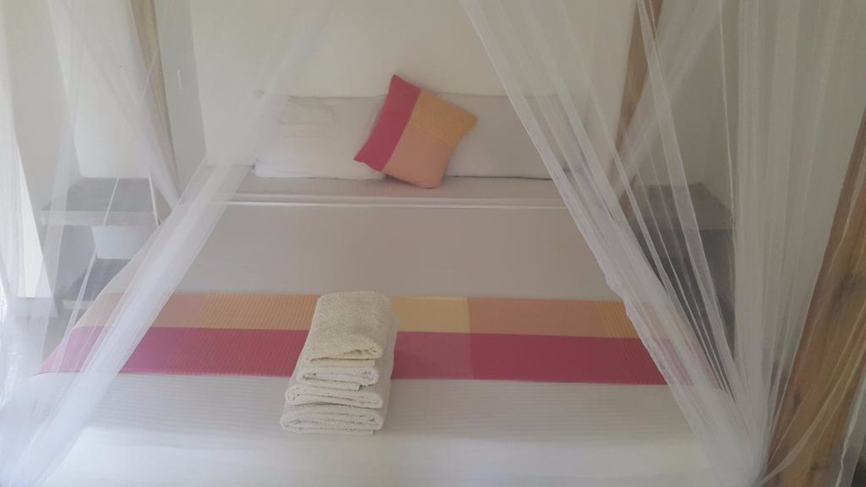 Una cama con mosquitero, una toalla doblada y una almohada.