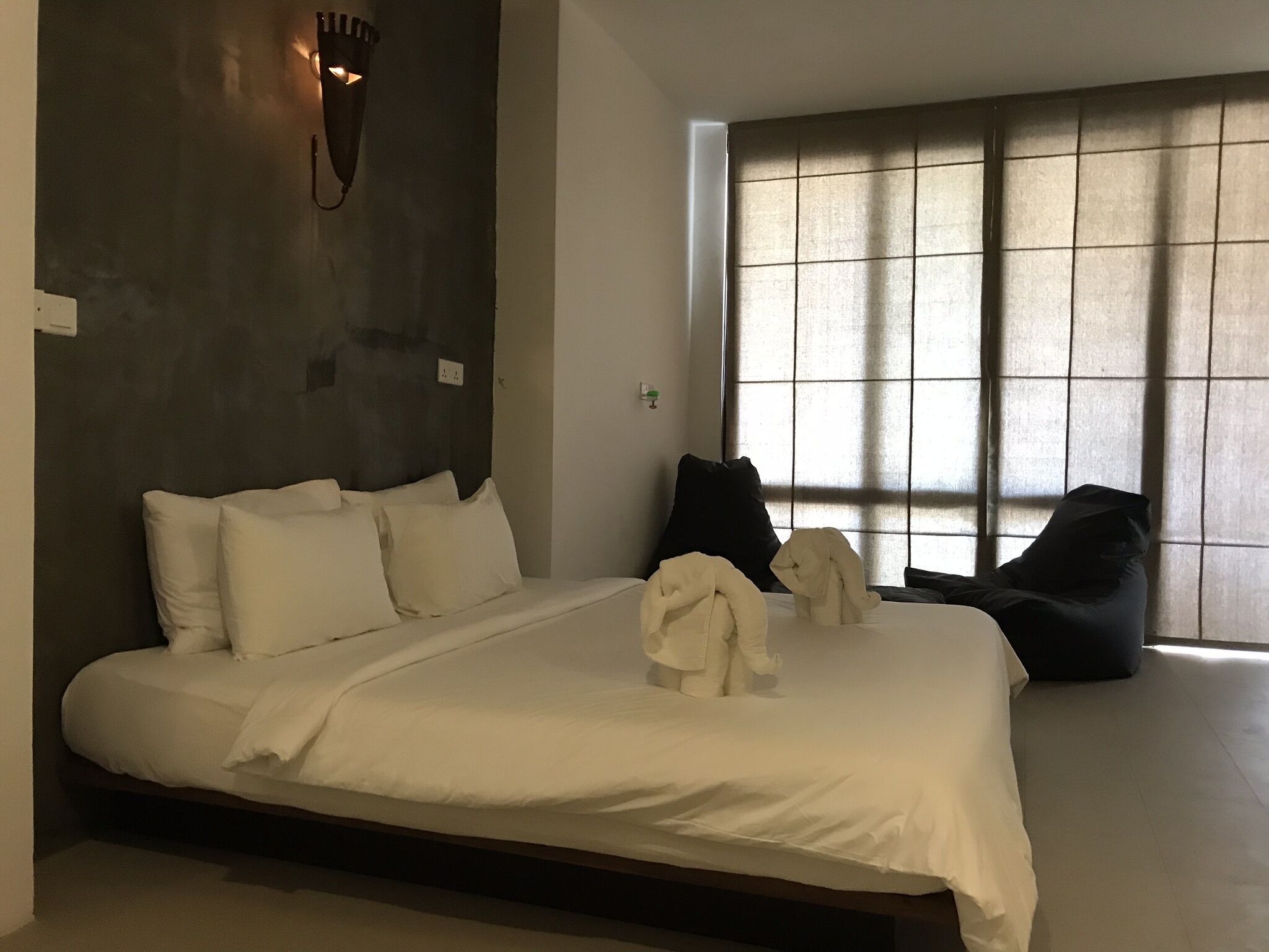 Un dormitorio moderno con una cama grande, una pared de acento oscura, una lámpara de pared y una ventana con persianas.