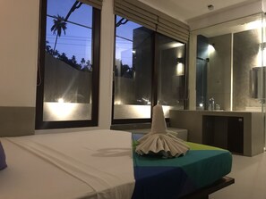 A hotel room with a bed, a bathroom with a mirror, and large windows.