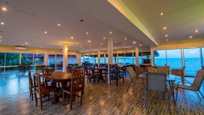 A spacious dining area with multiple tables and chairs, large windows offering ocean views, and a wooden floor. - Starlight Beach Resort Chumphon (Chumphon)