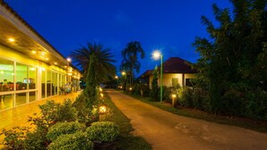 A well-lit pathway leading to a building with glass doors, surrounded by greenery and palm trees. - Starlight Beach Resort Chumphon (Chumphon)
