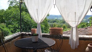 A patio with a round table and chairs, white curtains, and terracotta pots. - La Murata (Rapolano Terme)