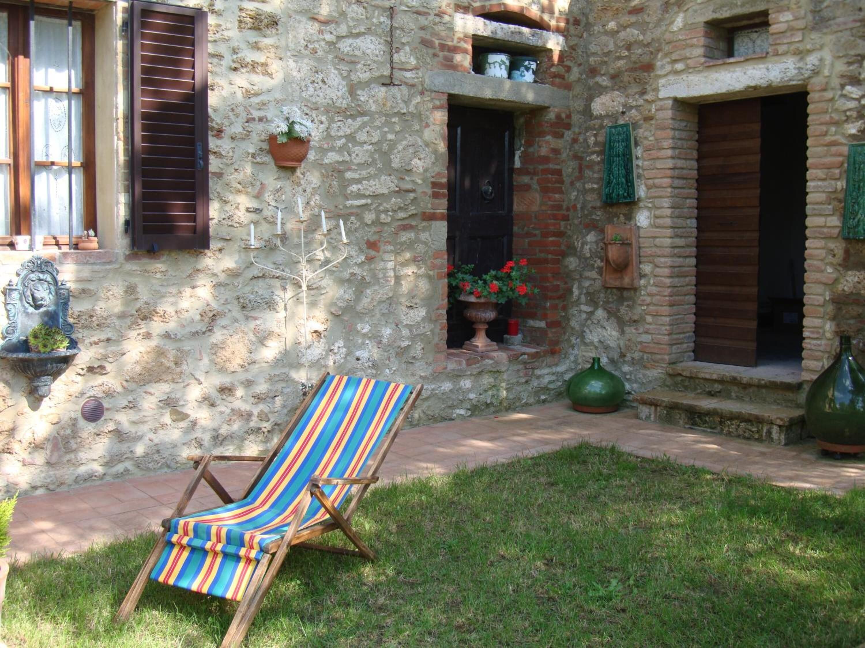 A stone building with a grassy courtyard, a striped chair, and a candelabra.