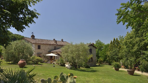A stone building with a tiled roof, surrounded by a well-maintained garden with various plants and a cactus in the foreground. - La Murata (Rapolano Terme)