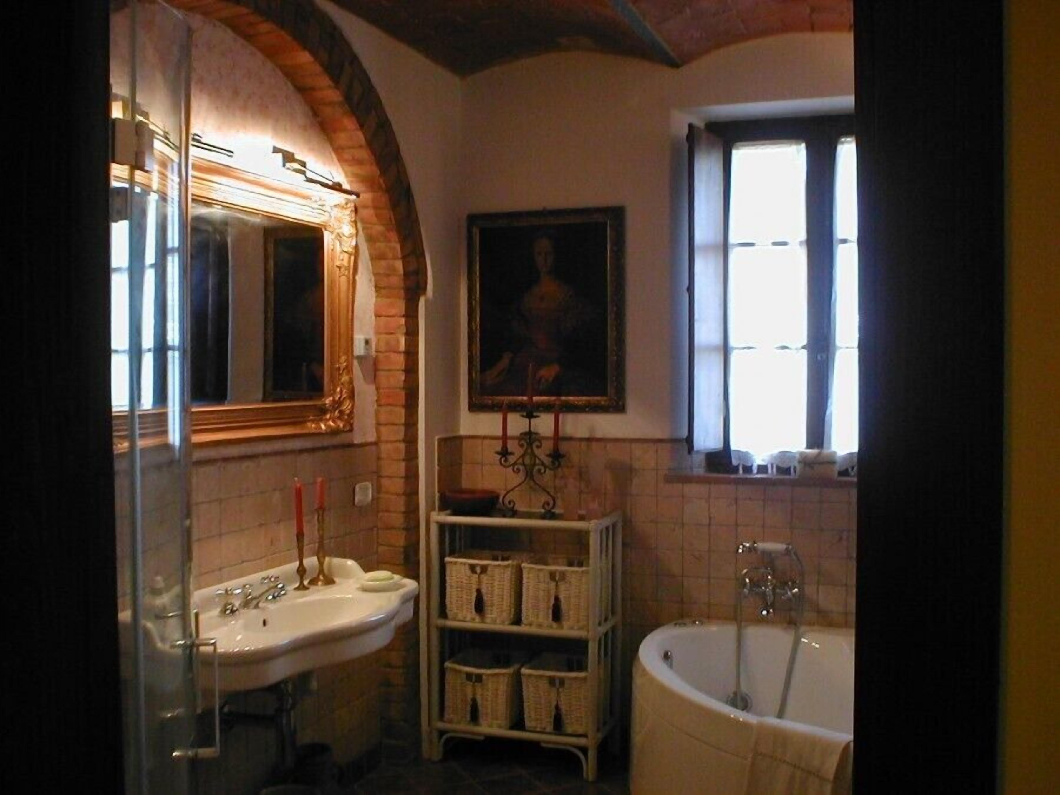 A traditional bathroom with a large arched mirror, a pedestal sink, a freestanding bathtub, and a window providing natural light.