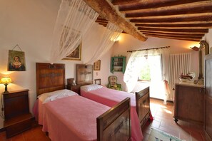 A bedroom with two beds, wooden furniture, a window with curtains, and a painting on the wall. - La Murata (Rapolano Terme)