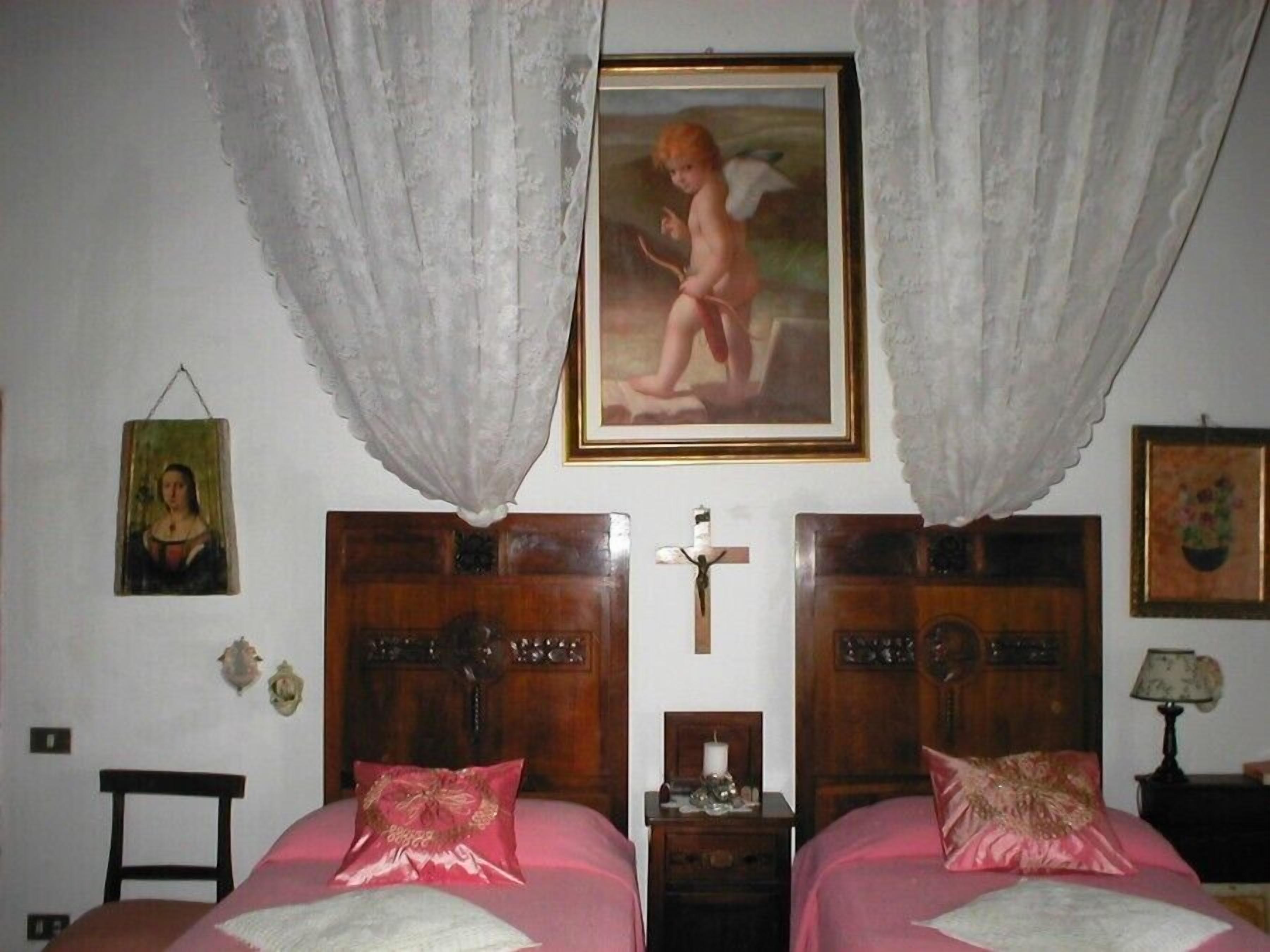 A bedroom with two beds, a cross on the wall, and a painting above the beds.
