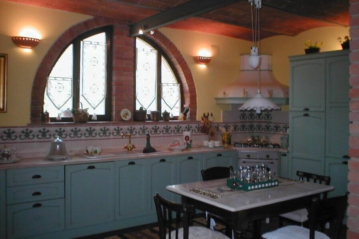 Una cocina con dos ventanas de arco, un salpicadero de azulejos y una zona de comedor con mesa y sillas.