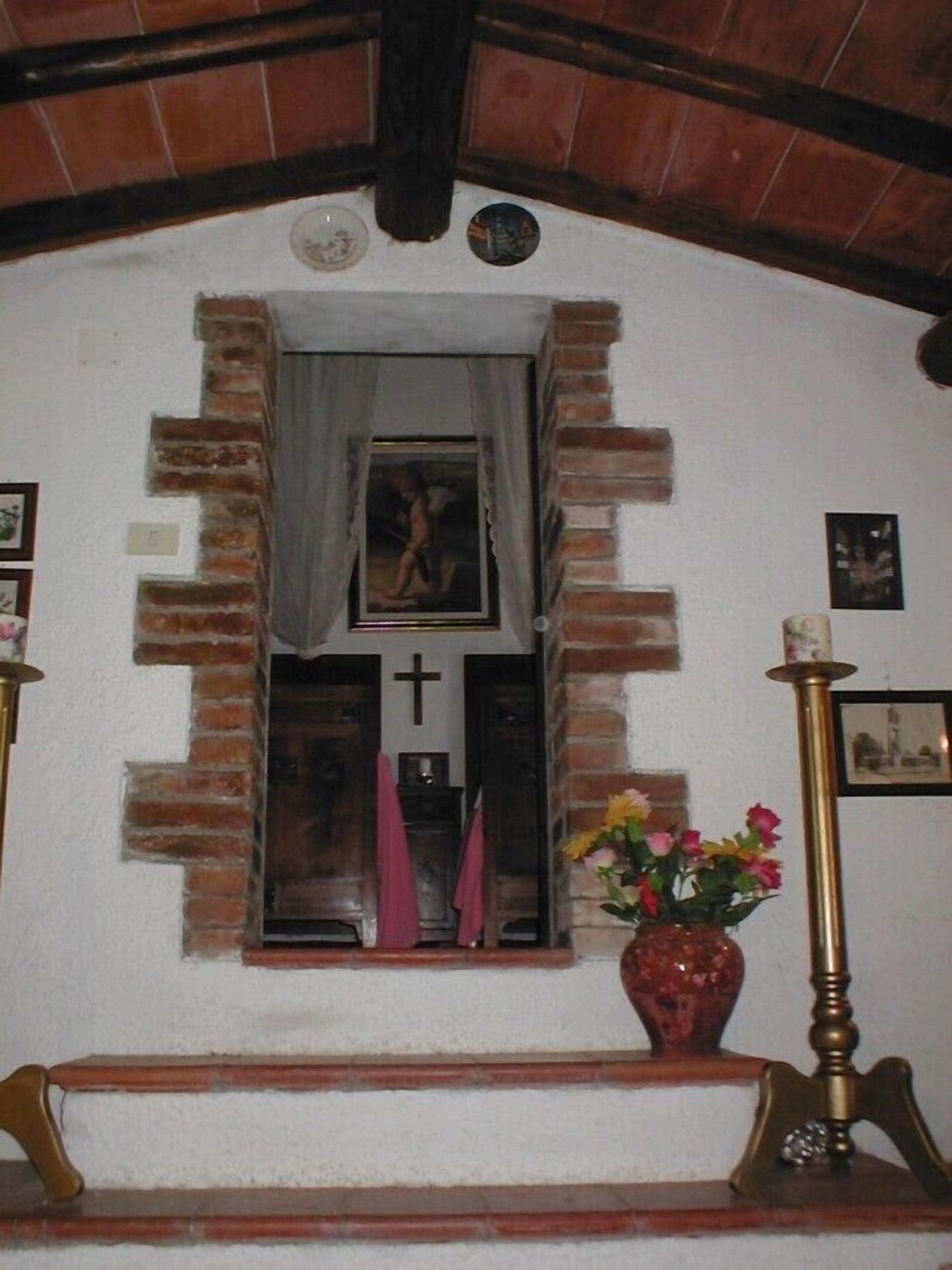 Una pequeña capilla con un banco de madera, un crucifijo y un jarrón con flores.