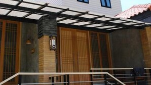 Un edificio de dos pisos con fachada blanca, un porche cubierto con barandilla negra y una pequeña escalera que lleva a la entrada.