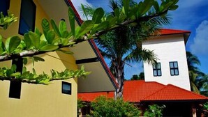 Un edificio de dos pisos con fachada amarilla y tejado rojo, rodeado de vegetación.