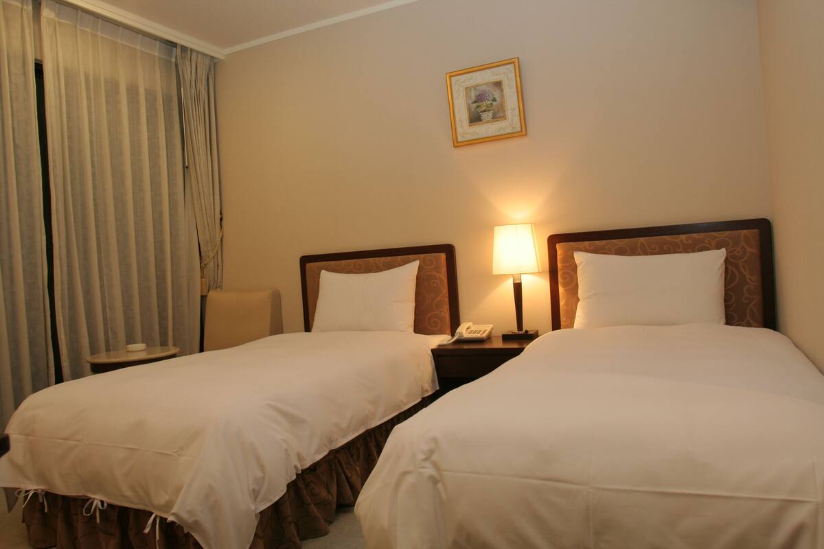 A hotel room with two single beds, a bedside table with a lamp, a phone, and a chair.