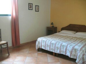 A bedroom with a bed, a nightstand, a chair, and a window with curtains. - Agriturismo La Torretta (Siena)