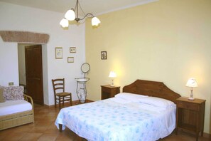 A bedroom with a bed, a chair, a small table with a lamp, and a wall-mounted shelf. - Agriturismo La Torretta (Siena)