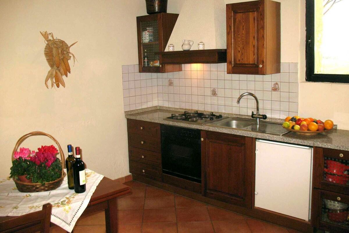 A compact kitchen with a sink, stove, and cabinets. There is a basket of flowers and bottles on the counter.
