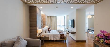Una habitación de hotel moderna con cama, sofá, televisor y un techo decorativo.