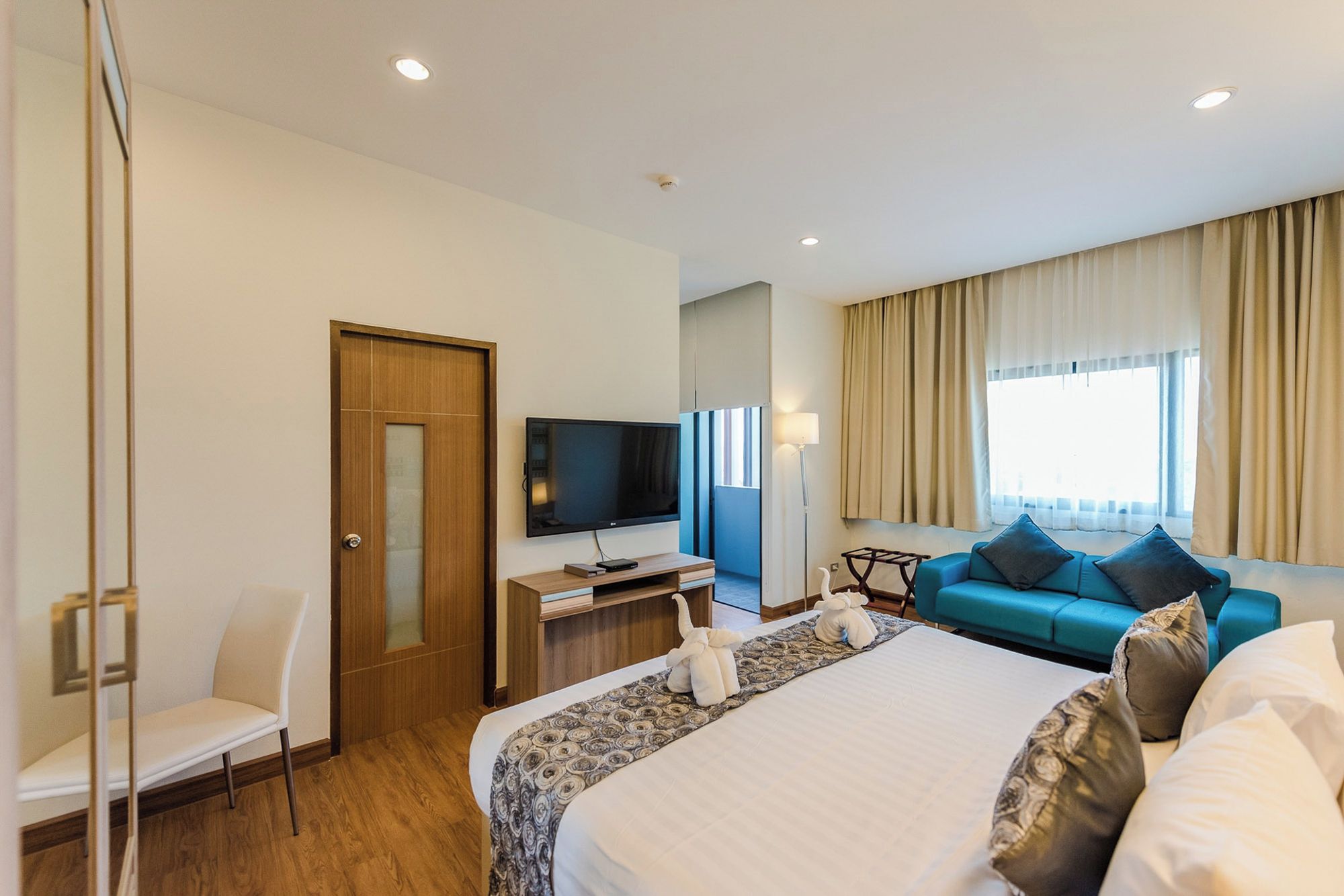 Una habitación de hotel con una cama, un escritorio con televisor, un sofá y una ventana con cortinas.