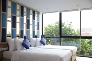 Habitación de hotel con dos camas, un ventanal grande y vistas a zonas verdes.