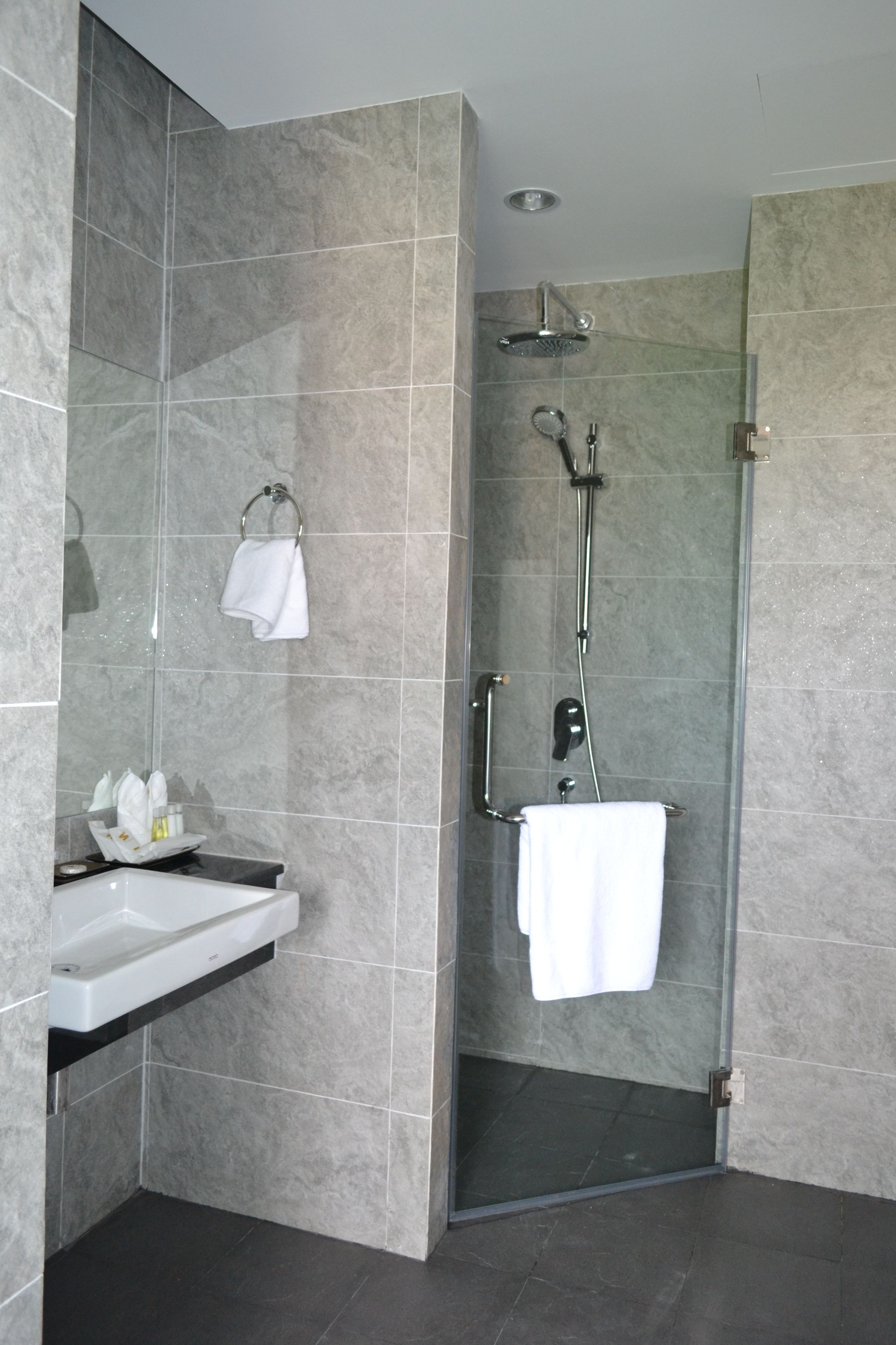 Un baño moderno con ducha envuelta en vidrio, un lavamanos con espejo y un perchero para toallas.