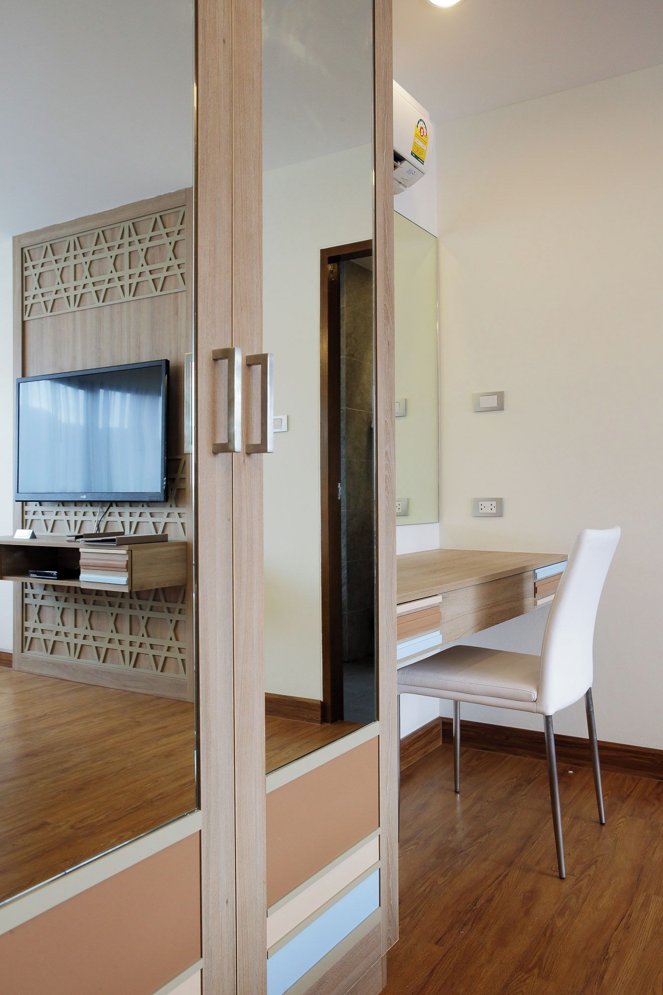 A modern interior with a wooden floor, a flat-screen TV mounted on a wall, a white chair, and a wooden desk with drawers.