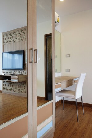 A modern interior with a wooden floor, a flat-screen TV mounted on a wall, a white chair, and a wooden desk with drawers. - S17 @ Nimman Hotel (Chiang Mai)
