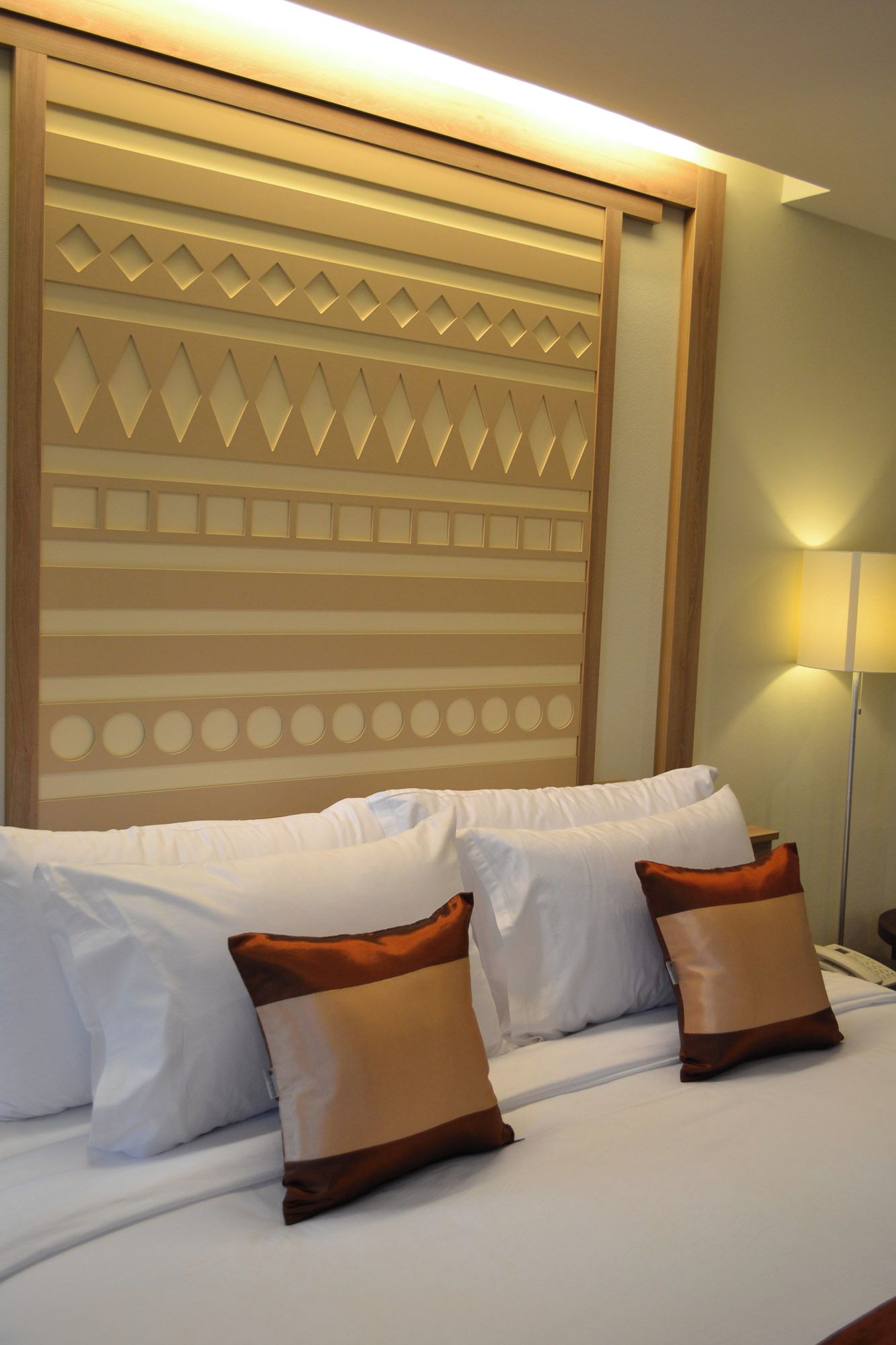 A hotel room with a bed, pillows, and a wall with a geometric pattern.