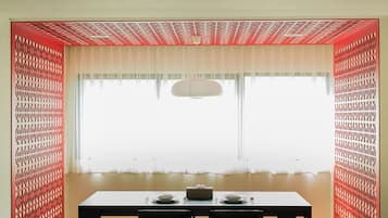 Un comedor con una mesa preparada para dos personas, dos sillas, un sofá y una ventana con vistas.