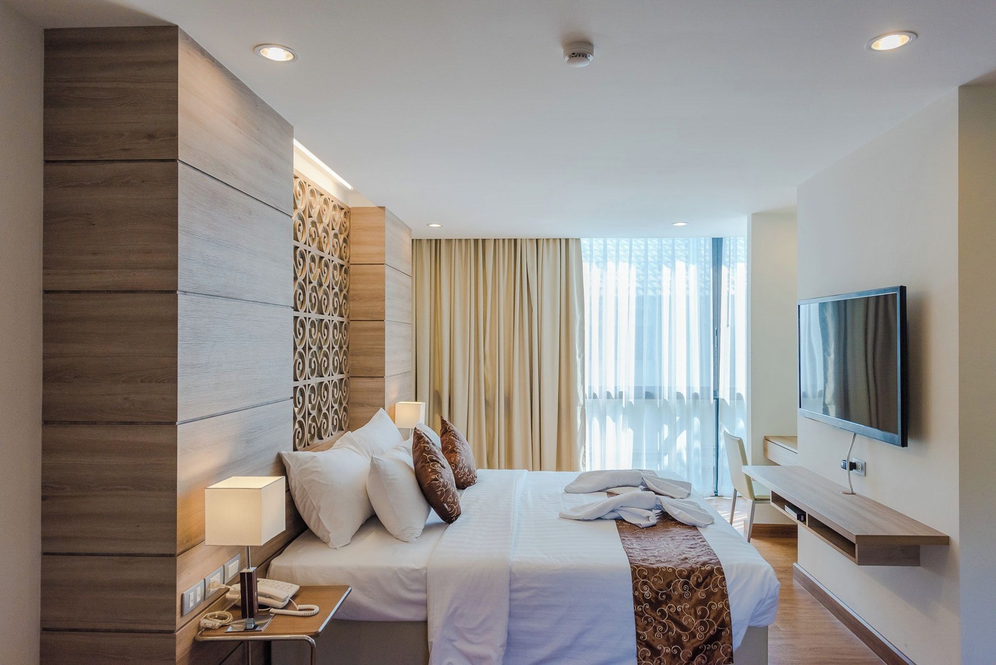 Una habitación de hotel moderna con una cama grande, televisión, escritorio y balcón con cortinas.
