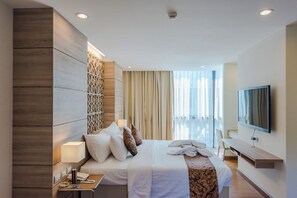 Una habitación de hotel moderna con una cama grande, televisión, escritorio y balcón con cortinas.