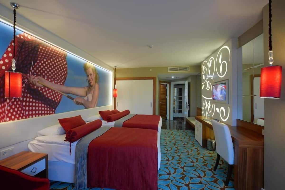A hotel room with a large bed, a desk, a mirror, and a TV.