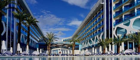 Um hotel moderno com piscina, vários andares e palmeiras.