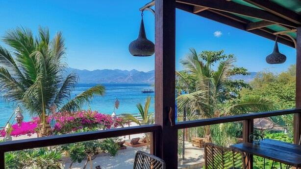 A balcony with wicker furniture, a view of the sea, and tropical plants.