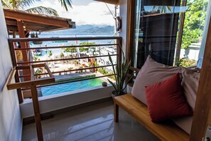 A balcony with a view of a pool and beach, a wooden bench, and a potted plant. - Pesona Beach Resort & Spa (Gili Trawangan)