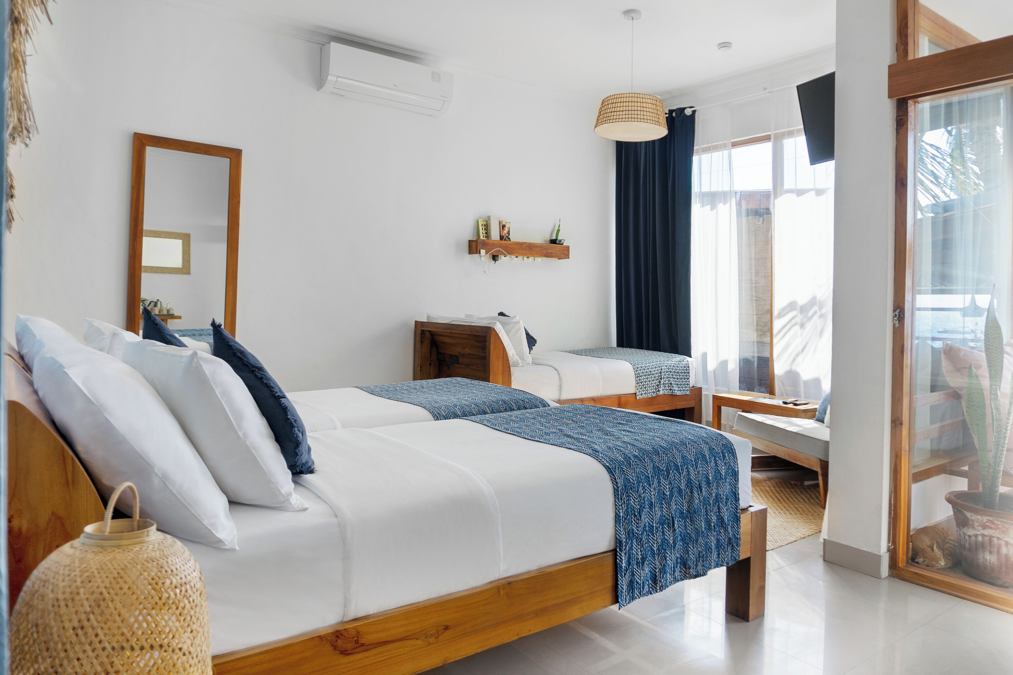 Un dormitorio moderno con dos camas, cabecero de madera, un escritorio pequeño y un ventanal con cortinas.
