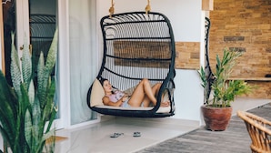 A room with a hanging chair, a potted plant, and a wooden floor.