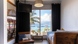 A bedroom with a large window, a bed, a bedside table, and a view of the ocean.