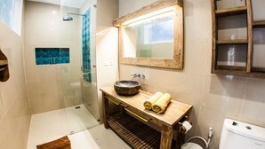 A modern bathroom with a glass shower enclosure, a wooden vanity with a sink, and a large mirror.