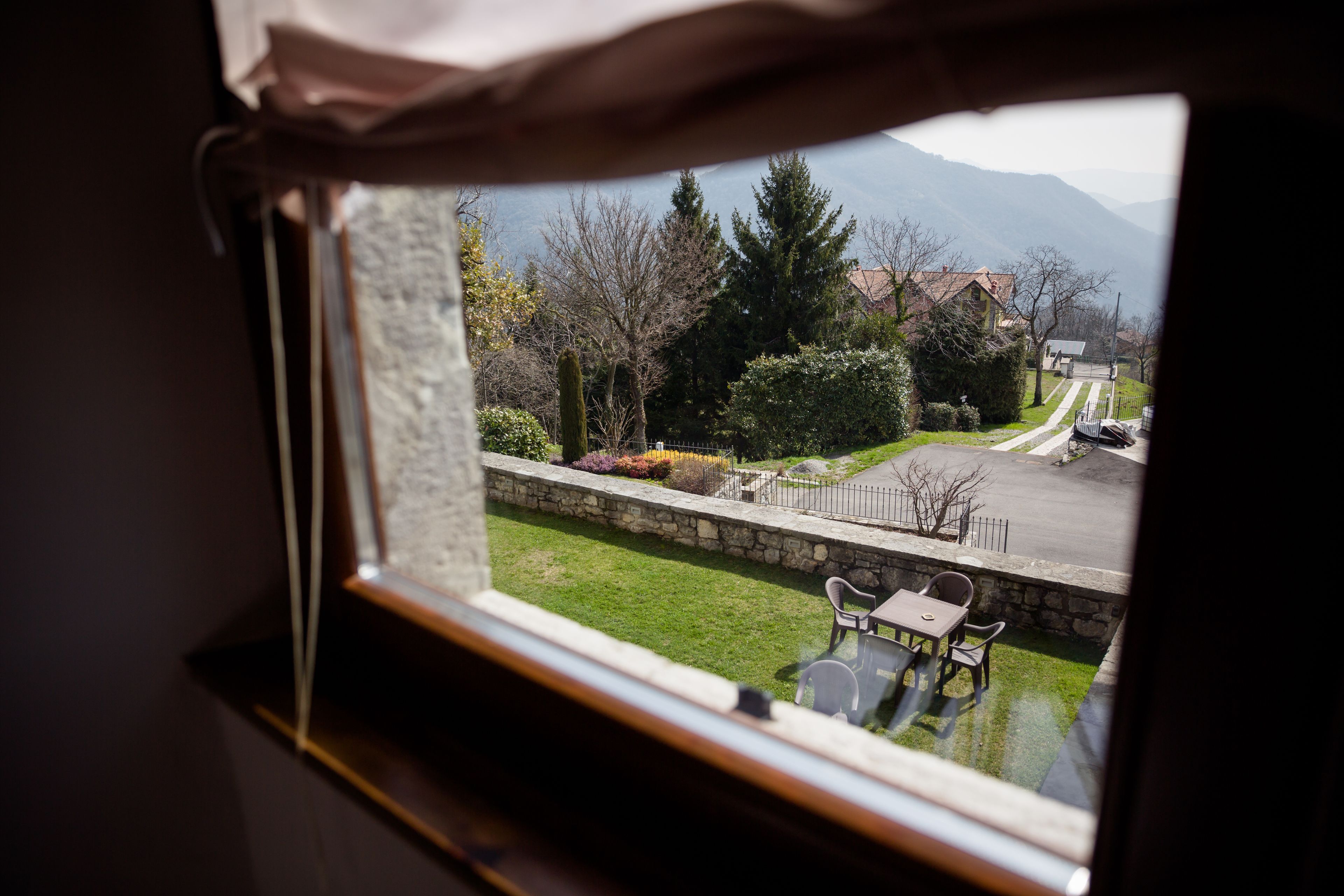 Une vue par la fenêtre sur une rue résidentielle, avec des maisons, un espace verdoyant et un mur de pierre.